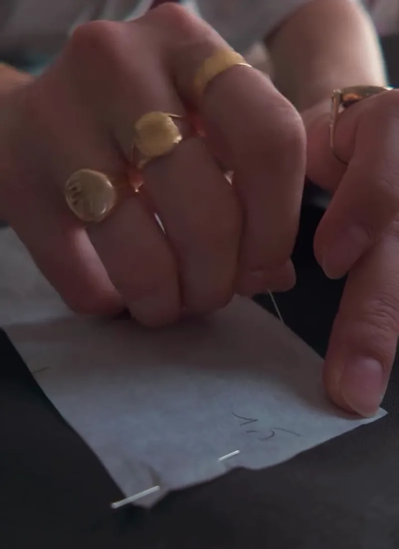 Mains baguées d'or qui cousent un patron sur tissu